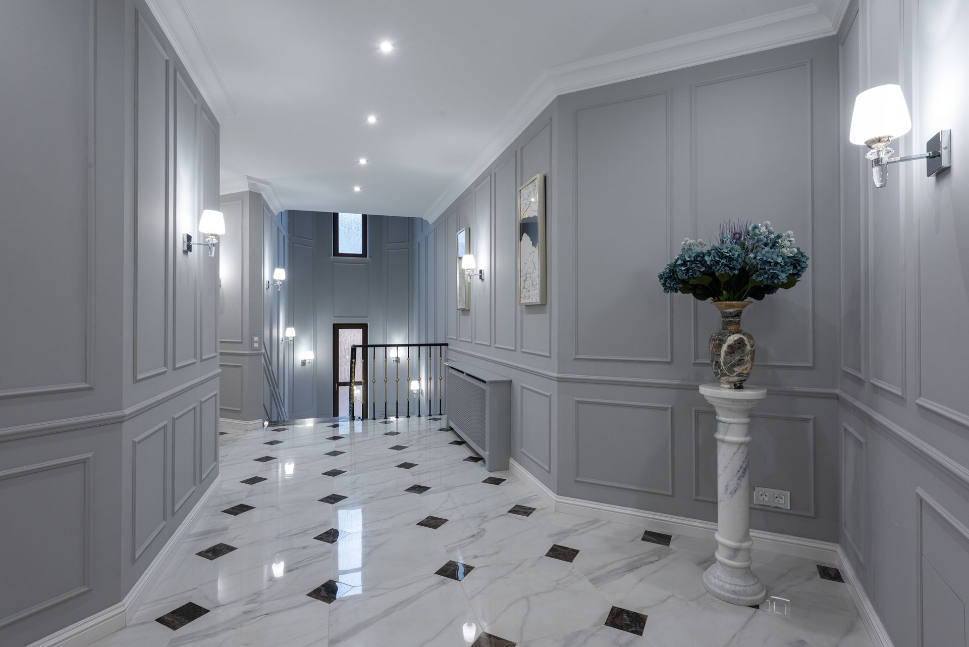 Gray walls and shiny marble floor in hallway of spacious classic styled villa decorated with paintings and lamps